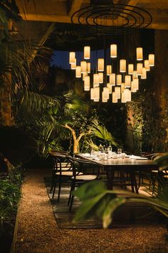 an outdoor dining area is lit up with lights and greenery on the walls, along with wooden tables and chairs