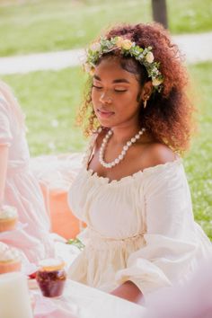 a woman in a white dress is sitting at a table with cupcakes on it