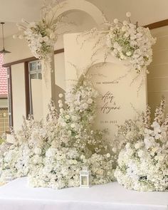 white flowers and greenery are arranged on a table in front of a wedding sign