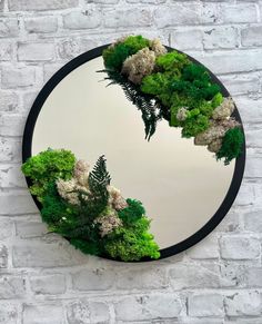 a circular mirror with plants and trees in the middle on a brick wall behind it