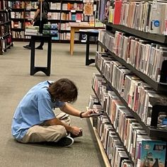 a man kneeling down in front of a book shelf filled with books