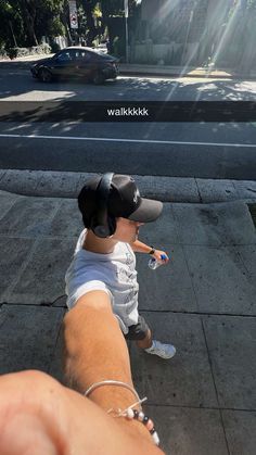 a small child wearing a hat riding on the back of a skateboard down a sidewalk