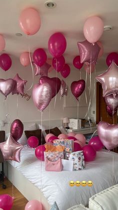 pink and silver balloons are floating in the air above a bed with white sheets on it