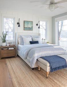 a bedroom with white walls and blue bedding in front of two large windows that overlook the water