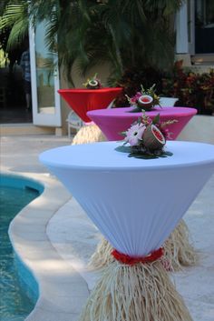 the table is decorated with pink and red vases on top of white tables near a swimming pool