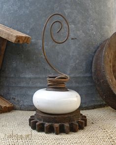 a white vase sitting on top of a wooden table next to a metal object with a spiral design