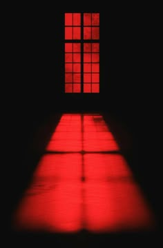 an empty room with red light coming through the window and shadows on the floor below