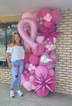 a woman standing in front of a balloon wall with pink balloons and stars on it