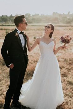 a bride and groom standing in the middle of an open field holding hands with each other