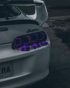 the front end of a white sports car with purple lights on it's bumper