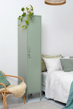 a green locker next to a bed and a chair in a room with white walls