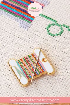 a needle and pin sitting on top of a piece of fabric next to a cross stitch pattern