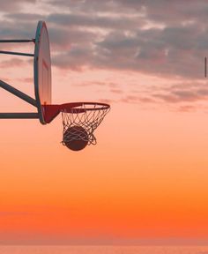 a basketball hoop is in the air above the water at sunset or dawn with an orange and pink sky