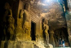 two people are standing in front of statues at the entrance to an underground cave temple