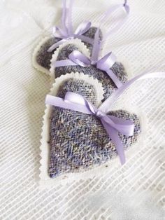 two heart shaped ornaments with purple ribbons on a white cloth background, one is made out of fabric and the other has a bow