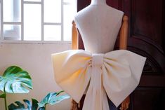 a mannequin wearing a white bow on top of a chair next to a potted plant