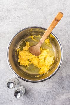 scrambled eggs in a saucepan with a wooden spoon next to it on a gray surface