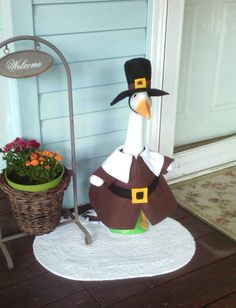 a duck wearing a pilgrim hat and standing next to a potted plant on the porch