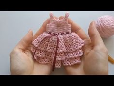 two hands holding a small pink crocheted dress and a ball of knitting yarn