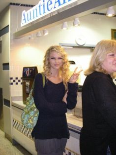 two women standing in front of a counter at an auto shop, one giving the peace sign