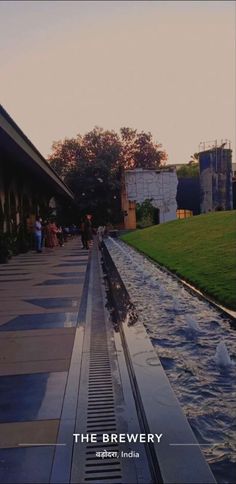 people are standing near the water in front of a building and some grass on the other side