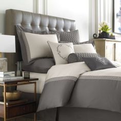 a bed with grey and white comforters in a bedroom next to a lamp on a night stand