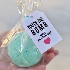 a hand holding a blue and green bath bomb with a tag that says, you're the bomb happy valentine's day