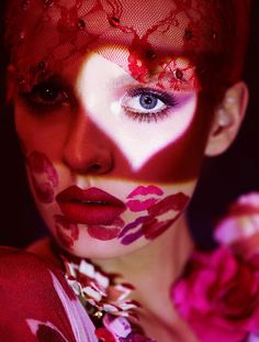 a woman with her face painted like a heart and red flowers on her chest is posing for the camera