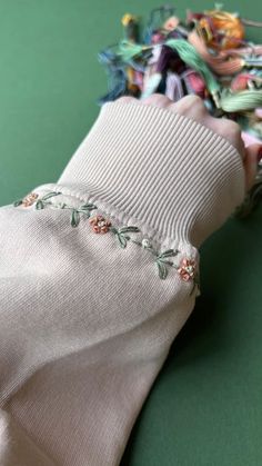 a hand is holding some fabric on top of a green surface with other items in the background