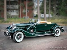 an antique green car parked on the side of the road in front of some trees