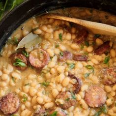 a pot filled with beans and sausages on top of a table next to a wooden spoon