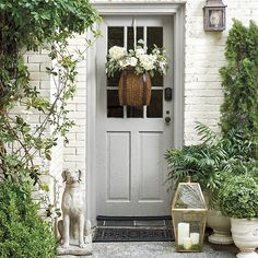 a white front door surrounded by greenery and potted plants with flowers in the basket