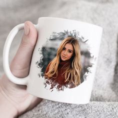 a hand holding a white coffee mug with a woman's face on it