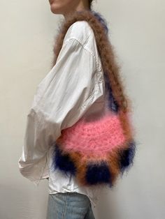 a woman is holding a handbag made out of yarn and felts, in front of a white wall