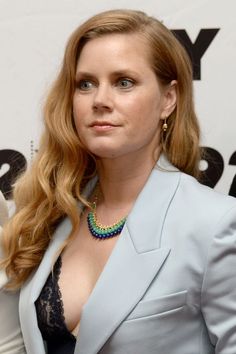 a woman with long hair wearing a blue suit and green beaded necklace, posing for the camera