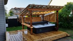 a hot tub on a wooden deck in a backyard with a pergolated gazebo