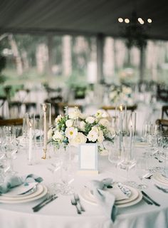 the table is set with white flowers and silverware for an elegant wedding reception in a tented area