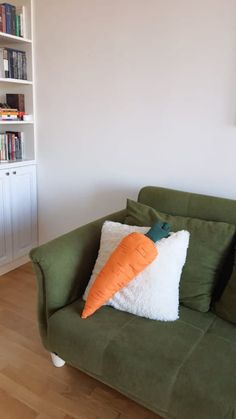 a green couch with a carrot pillow sitting on it's back in front of a bookshelf