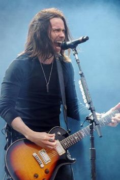 a man singing into a microphone while holding a guitar in front of him and his mouth open