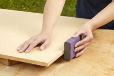 a person using a sanding block on a piece of plywood board with their hands