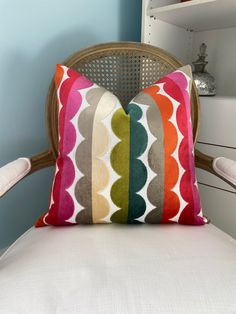 a colorful pillow sitting on top of a white chair next to a book shelf and dresser