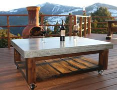 a table on a deck with wine glasses and bottles in front of an outdoor fireplace