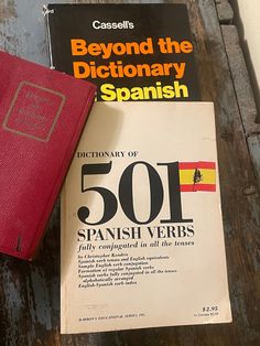 a book sitting on top of a wooden table next to a red wallet and a spanish dictionary