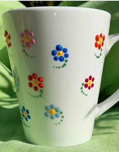 a white coffee cup with colorful flowers painted on the outside and inside, sitting on a green surface