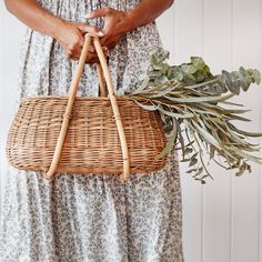 a woman holding a wicker basket with greenery