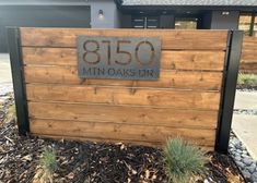 a sign that is on the side of a fence in front of a house with grass and rocks