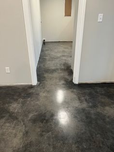 an empty room with white walls and gray flooring is seen from the doorway to the hallway