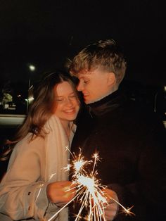 a man and woman standing next to each other holding sparklers