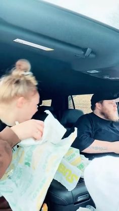 a man and woman sitting in the back seat of a car, one holding a napkin