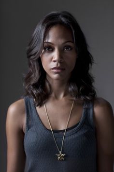 a beautiful young woman wearing a necklace with a cross on it's neck and looking at the camera